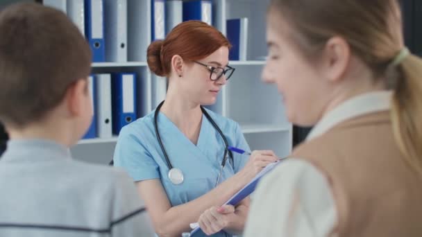 Πορτρέτο του ευτυχισμένου γιατρού με μπλε στολή στο γραφείο του νοσοκομείου, οικογενειακός γιατρός γράφει μια συνταγή για τη θεραπεία των ασθενών κατά τη διάρκεια μιας διαβούλευσης στην κλινική — Αρχείο Βίντεο