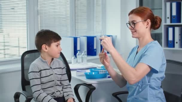 Salute e medico, medico di sesso femminile in uniforme blu e occhiali da digitare vaccino con siringa poi inietta il paziente ragazzo in ufficio ospedaliero — Video Stock