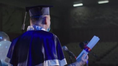 Akademik manto erkek öğretim görevlisi r ve tıp maskeli şapka konferans odasındaki video bağlantısı yoluyla mezunlara diplomaları sunuyor
