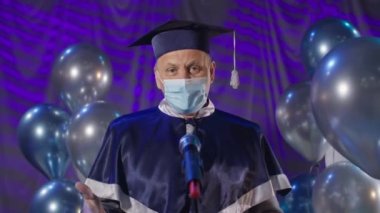 Yüz maskesi takan erkek rektör güvenlik önlemlerini izliyor ve diplomasını sosyal uzaklık sırasında video bağlantısı yoluyla İnternet 'te sunuyor