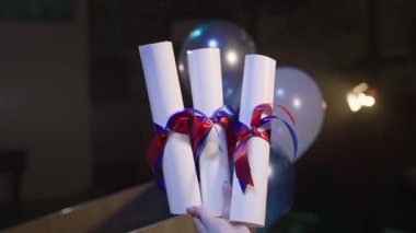 Mezuniyet sertifikası elinde balonların kırmızı ve mavi kurdelesi ve spot ışıklarının ışığı, yakın plan