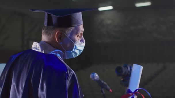 Profesor universitario en ropa académica y sombrero está presentando diplomas utilizando tecnologías modernas a través de la comunicación por vídeo en la sala de conferencias — Vídeos de Stock