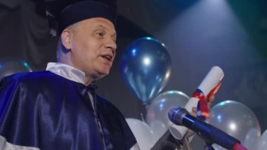 Mantodaki erkek öğretmen mikrofonun konferans salonunda diploma töreni düzenliyor.