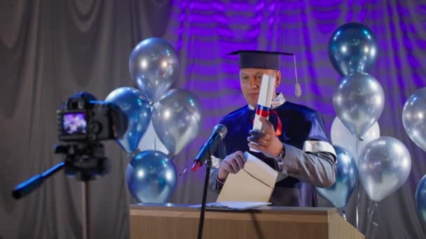 Instituer professeur en manteau félicite les diplômés à la fin de l'année scolaire en ligne avec l'aide des technologies modernes fond de ballons — Video