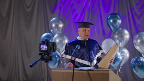 Muž univerzitní učitel šťastně gratuluje absolventům na konci akademického roku a představuje diplom on-line prostřednictvím živého vysílání a video odkaz v konferenčním sále — Stock video