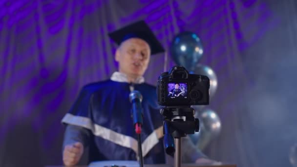 Профессор университета в мантии поздравляет выпускников с окончанием учебного года онлайн по видеосвязи — стоковое видео