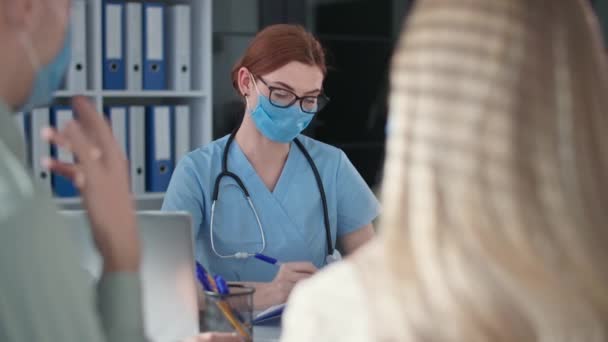 Trabajador médico con fonendoscopio y máscara médica para protegerse contra virus e infección examina pareja casada en consultorio de clínicas — Vídeo de stock