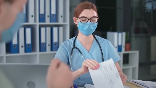 Kadın doktor, fonendoskop ve virüs ve enfeksiyona karşı koruyucu maske ile hastane ofisindeki hastalara negatif koronavirüs testi gösteriyor. — Stok video