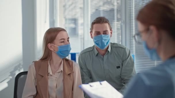 Hombre y mujer con máscaras protectoras en la cara debido al virus peligroso, hablando con la terapeuta durante la consulta con el médico en la clínica — Vídeo de stock