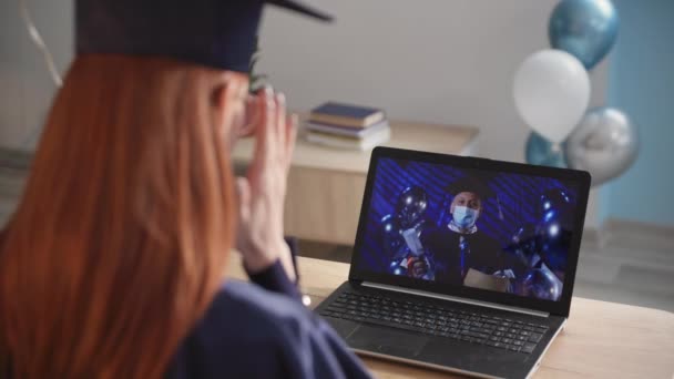 Jovem estudante em traje acadêmico celebra graduação on-line via link de vídeo no laptop durante a educação a distância — Vídeo de Stock