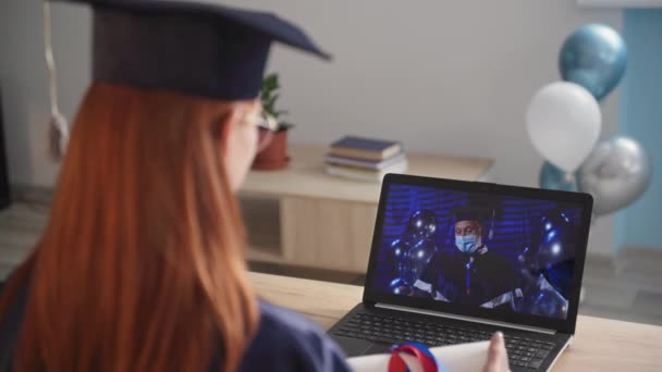 女学生通过笔记本电脑视频链接获得大学教育证书，在大流行病期间，男教师戴着医疗面罩 — 图库视频影像
