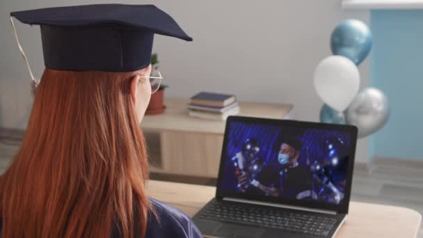 Junge entzückende Studentin in akademischer Kleidung besucht Online-Graduierung mit männlichen Lehrer mit medizinischer Maske, verwendet Universitätsrektor moderne Video-Kommunikationstechnologie, um den Abschluss während — Stockvideo