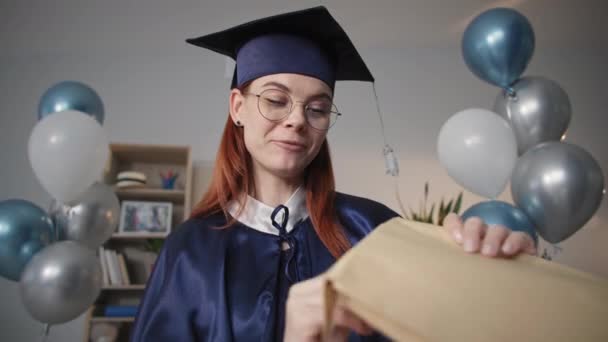 Emotional girl in academic dress rejoices at getting her university degree online and talks by video call on laptop during social distance and distance learning — Wideo stockowe