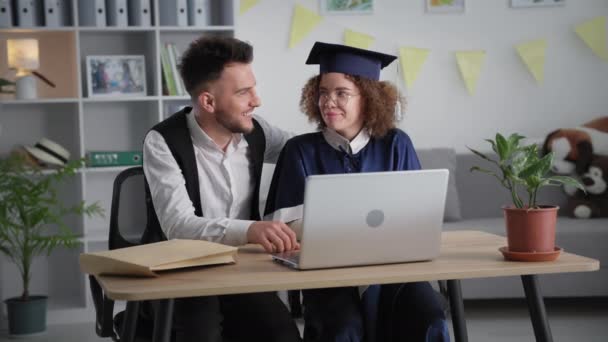 Aprendizaje a distancia, joven estudiante con el hombre se regocija por el diploma recibido en línea durante la ceremonia virtual a través de enlace de vídeo en el ordenador portátil — Vídeos de Stock
