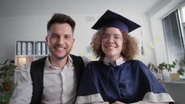 online graduation, happy female university graduate student with her husband at ceremony to receive education certificate by video communication on laptop while sitting at home