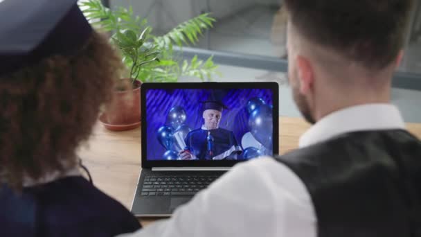 Graduación en línea, estudiante en traje académico relojes ceremonia diploma felicitaciones junto con el hombre que utiliza la tecnología moderna de comunicación de vídeo en el ordenador portátil — Vídeo de stock