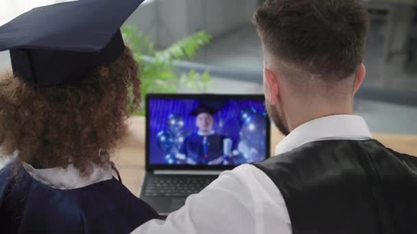 Studio a distanza, laureata donna in mantello accademico e cappello orologi cerimonia di laurea insieme al fidanzato utilizzando la moderna tecnologia di comunicazione video sul computer — Video Stock