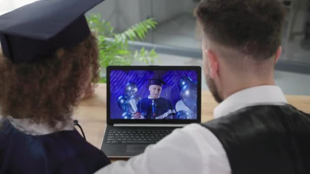 학교에서 비디오 컨퍼런스를 통해 남자 교사와 함께 온라인으로 졸업을 하는 젊은 부부 — 비디오