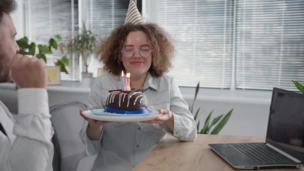 Віртуальна вечірка, радісний чоловік і щаслива молода жінка з вечірньою кепкою, що дме свічки на торт під час дня народження і спілкування з друзями через відео — стокове відео