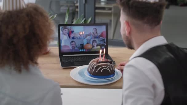 День рождения онлайн, счастливый муж и жена с шапками на голове и торт со свечами, празднующих вечер с друзьями по видеосвязи — стоковое видео