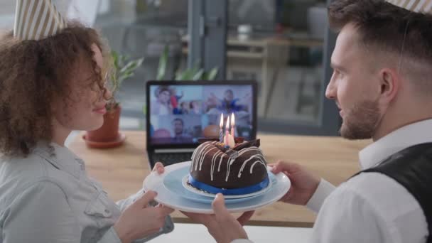 Party online, happy man and woman with caps on their heads and cake with candles celebrating birthday with friends via video link sitting at home — Stockvideo