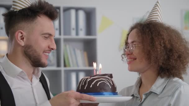Чарівна пара з кепками на голові робить бажання і вибухає свічки на день народження торт святкування річниці або дня народження вдома — стокове відео