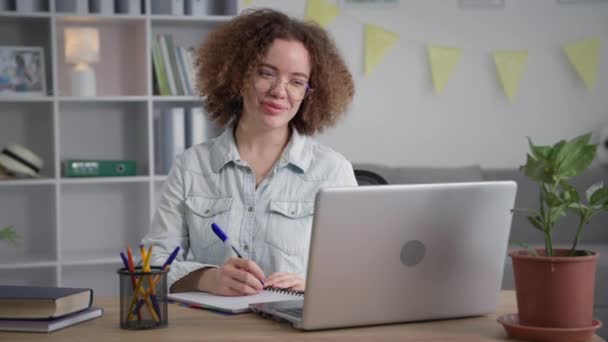 Distance learning, female student with glasses undergoes online training and communicates with instructor via video communication on laptop while sitting at home — Stock video