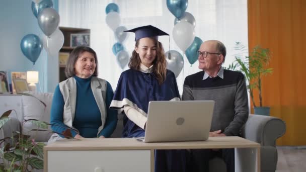 Щасливі батьки вручають дипломи своїй доньці під час урочистої церемонії онлайн через відеозв'язок на ноутбуці, сидячи вдома, пандемія — стокове відео