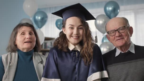 Diplômée dans un chapeau académique et robe avec des parents heureux célébrant la graduation en ligne en ligne par voie de connexion, regardez la caméra — Video