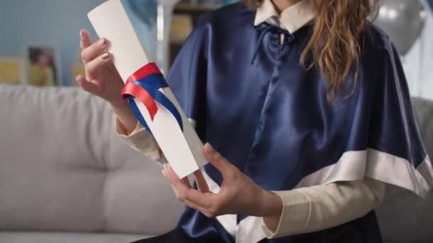 Remote learning, young female student in academic attire enjoying graduation and holding diploma — Stockvideo