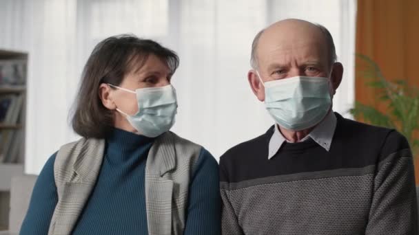 Pandemia, pareja de ancianos en máscaras médicas utilizar tecnologías modernas y comunicarse con el médico que atiende en línea a través de la webcam en el ordenador portátil — Vídeo de stock