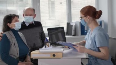 elderly man and woman wearing medical masks to protect against virus and infection in consultation with female attending physician during treatment in hospital office