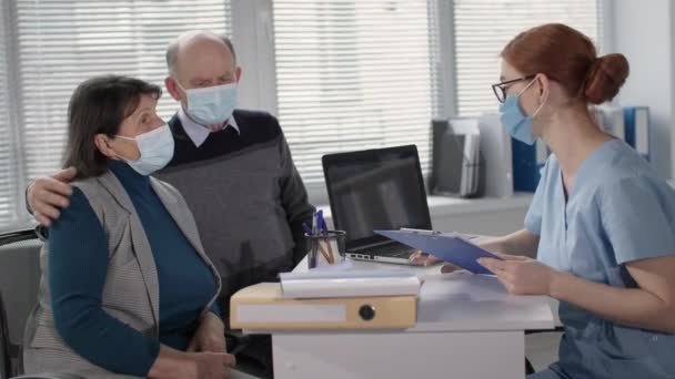 Ältere Rentner in medizinischer Maske während der Pandemie wegen gefährlichen Virus und Krankheit an der Rezeption der Ärztin — Stockvideo