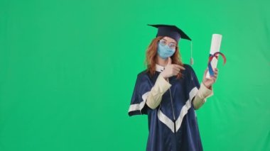 Karantina eğitimi, akademik kıyafetler ve tıbbi maske ile mezun olmak diplomayı parmağıyla gösteriyor, sonra parmak yukarı ve el ele vererek yeşil arka planda duruyor, kroma anahtarı.