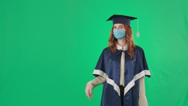 Graduación en cuarentena, graduado universitario se regocija en el diploma y muestra de mano a lado para la inscripción, mientras que de pie en el fondo de pantalla verde — Vídeo de stock