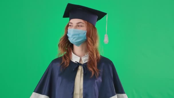 Diploma on-line, graduado em máscara médica se alegra com certificado recebido de educação e aponta os dedos para cima durante a distância de aprendizagem fundo tela verde, chave chroma — Vídeo de Stock