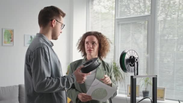 Moderne Technologien, junge kreative Männer und Frauen mit einer Spule Kunststoff für den 3-D-Drucker in der Hand diskutieren im Raum das Layout des Produkts — Stockvideo