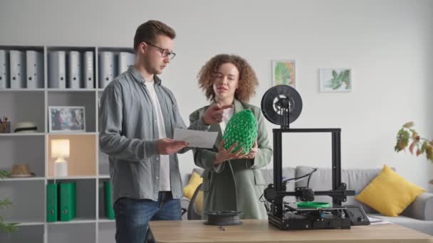 Портрет креативных инженеров мужского и женского пола, изучающих проект и детали, выполненные на 3D принтере в домашней обстановке для дизайна и улучшения дома — стоковое видео