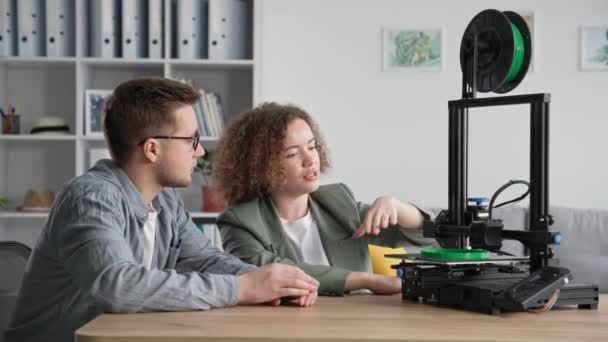 3D-modellering, jong stel man en vrouw studeren 3D-printen thuis en kijken naar het werk van 3D-printer zitten aan tafel in de kamer — Stockvideo