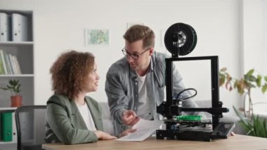 Modern modelleme teknolojileri, yakışıklı genç adam ve kadın 3D yazıcının çalışmalarını evde 3D model yazarken izliyorlar.