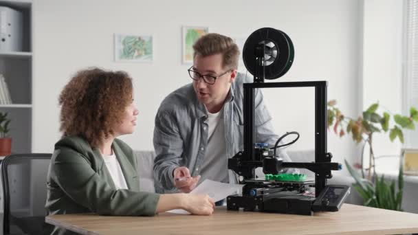 Ritratto giovane talentuoso team di lavoro uomo e donna stanno discutendo la stampa prototipo su stampante 3d a casa, sorridendo e guardando la fotocamera — Video Stock