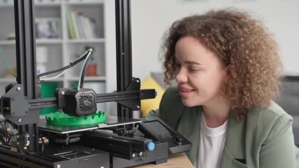 Charmante jonge vrouwelijke ontwerper ingenieur maakt gebruik van moderne technologie en houdt toezicht op 3D-printer tijdens het afdrukken prototype thuis — Stockvideo