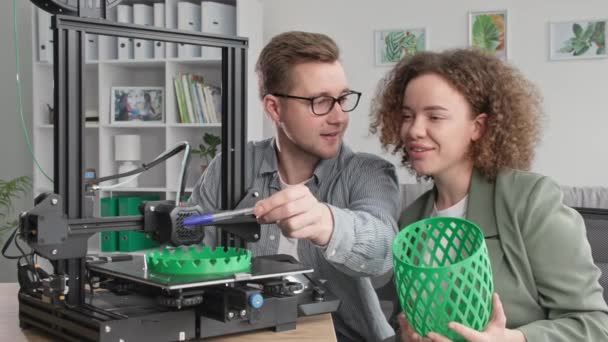 Technologische vooruitgang, moderne man en lachend meisje kijken graag naar het afdrukken van prototype 3D-printer thuis — Stockvideo