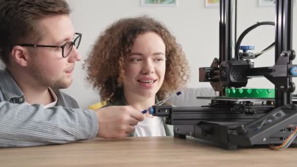 Parejas de jóvenes talentosos hombres y mujeres utilizan la tecnología moderna y supervisan el proceso de creación de un prototipo de un modelo 3D en una impresora 3D en casa — Vídeos de Stock