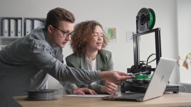 Profesyonel erkek ve kadın çiftler modern teknolojiyi kullanır ve bir dizüstü bilgisayar üzerinde çalışarak evdeki 3D yazıcı için 3D bir prototip tasarlarlar. — Stok video