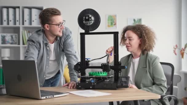 Jonge creatieve mannelijke en vrouwelijke ingenieurs maken een 3D-model op een laptop voor het afdrukken op een 3D-printer thuis — Stockvideo