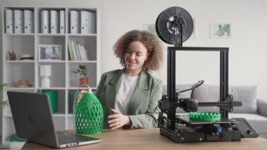 Evde geliştirme, 3 boyutlu abajur modeli prototipi olan yaratıcı kadın tasarımcı evde 3D baskı yazıcısında, gülümsüyor ve kameraya bakıyor.