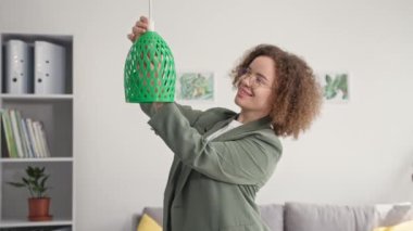 Modern teknolojiler, gözlüklü çekici kadın lambayı 3D yazıcıya basılmış abajur modeline dönüştürüyor, gülümsüyor ve kameraya bakıyor.