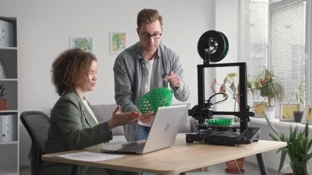 Evde yaratıcı işler, genç adam ve kadın modern teknolojiyi kullanıyor ve oturma odasındaki 3 boyutlu yazıcıya 3 boyutlu bir modelin prototipini basıyor. — Stok video
