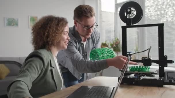 Ev için modern teknolojiler, gülümseyen adam ve kadın oturma odasında oturan 3D baskı makinesini kullanarak bir 3D modelin prototipini basıyor. — Stok video
